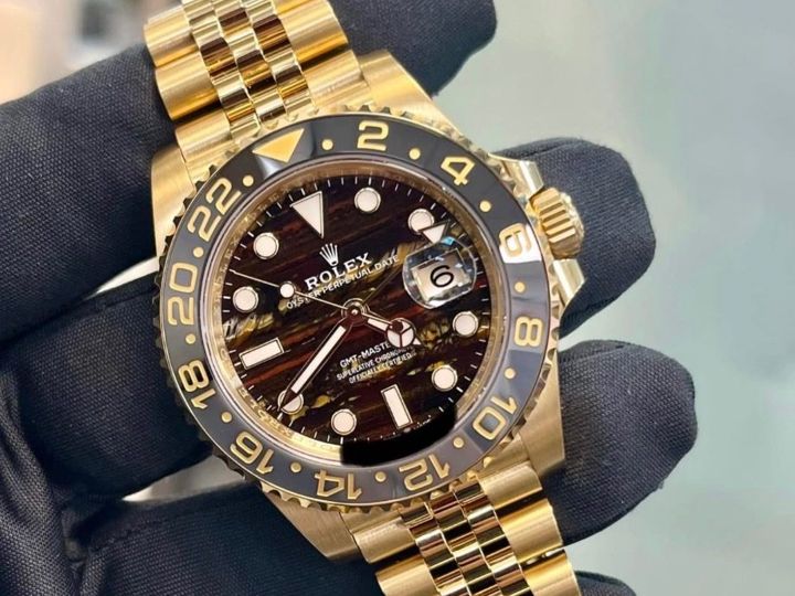 A gloved hand holding a yellow gold Rolex GMT-Master II on a Jubilee bracelet