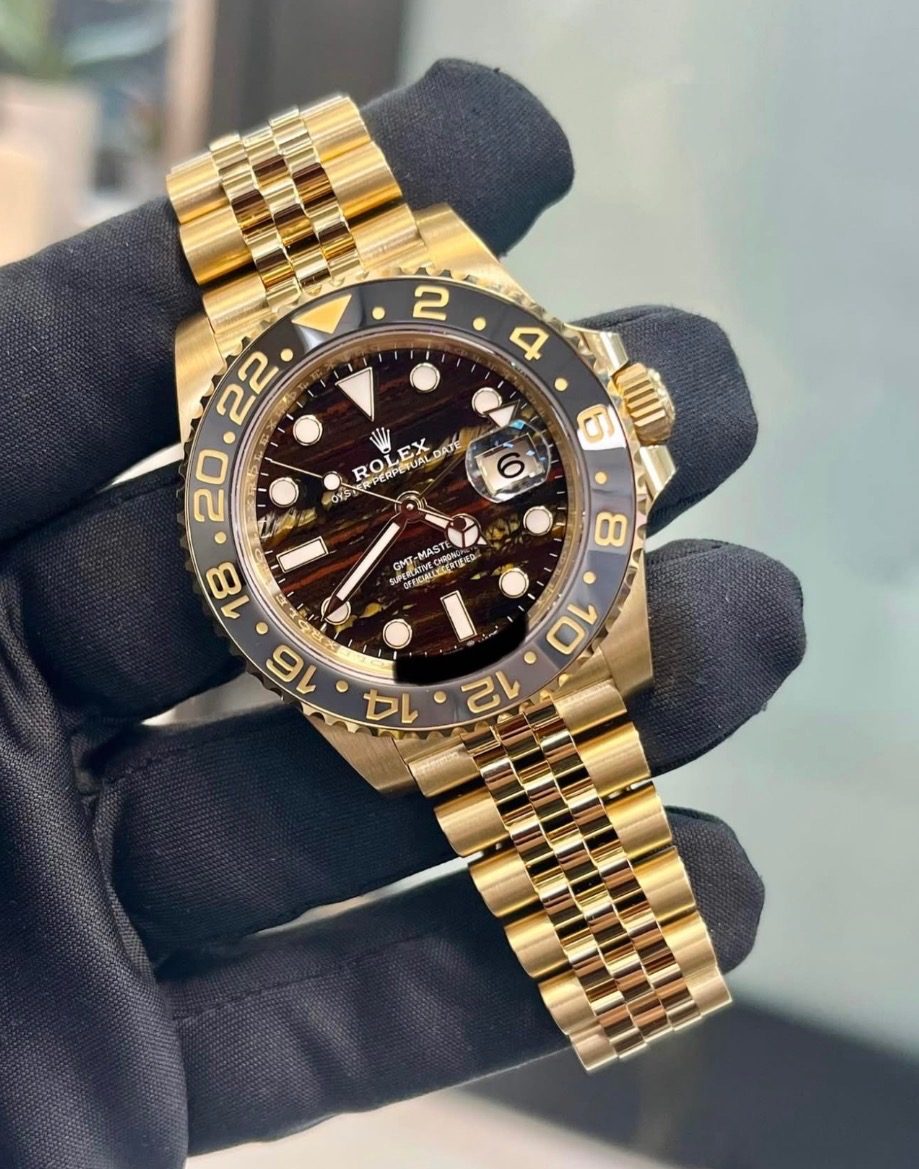A gloved hand holding a yellow gold Rolex GMT-Master II on a Jubilee bracelet