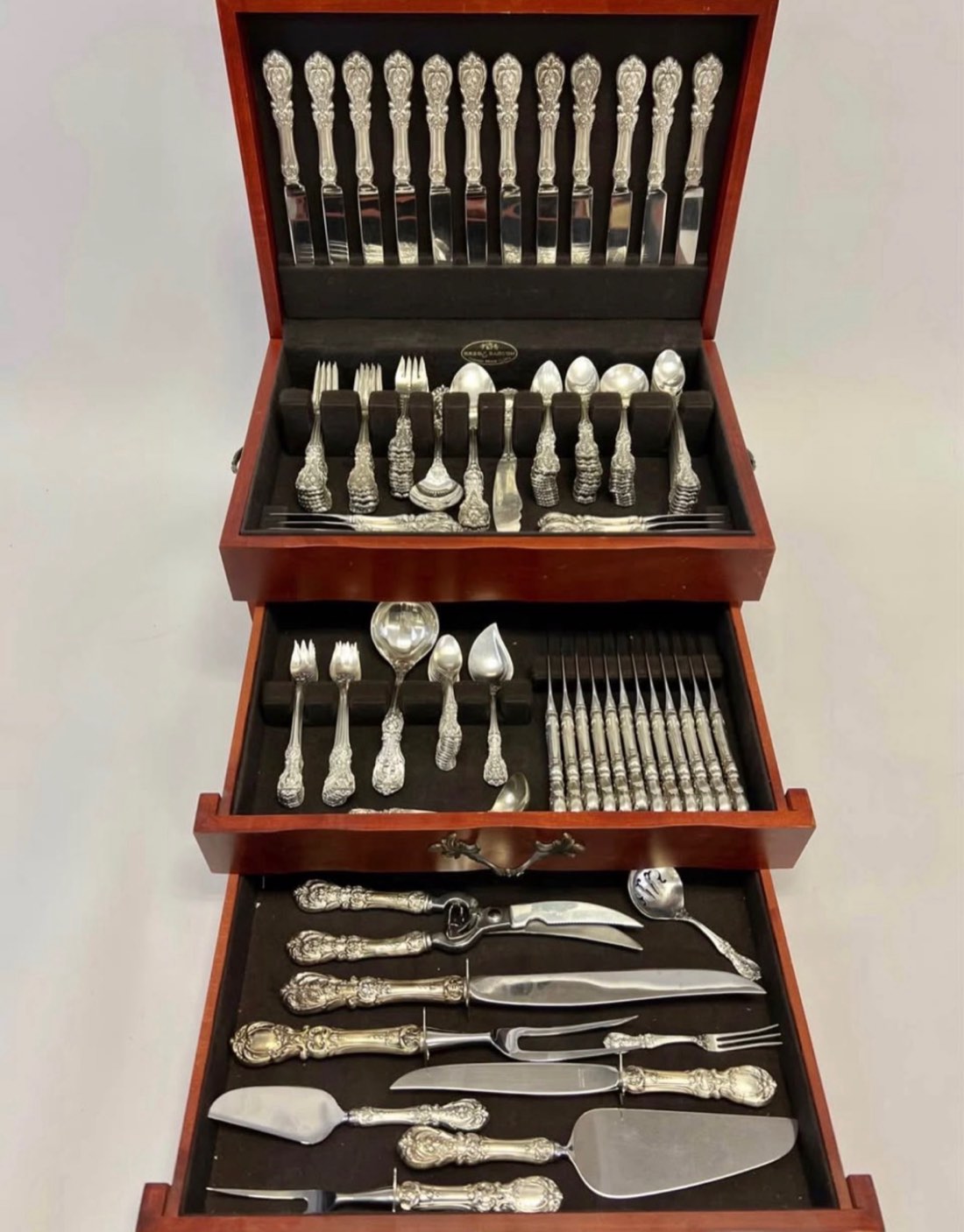 Ornate silver flatware arranged in an open wooden chest.