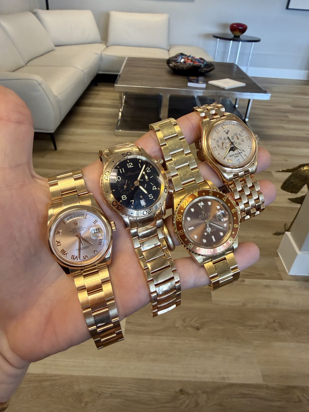 A hand holding four gold and two-tone luxury wristwatches